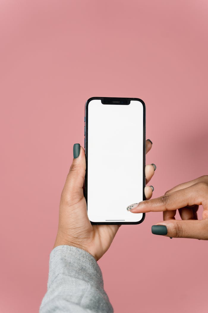 Mastering the First Impression: Your intriguing post title goes here Close-up of hands holding a smartphone with a blank screen against a pink background.